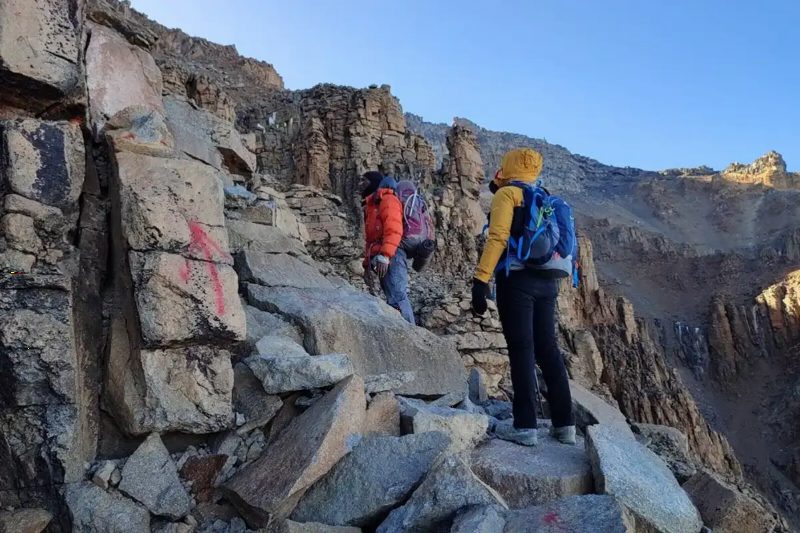 Two climbers in bright jackets scrambling up a steep rock face.