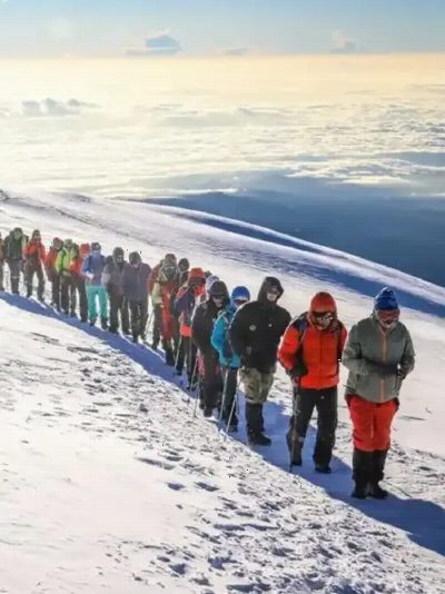 A line of climbers crossing snow above the clouds.
