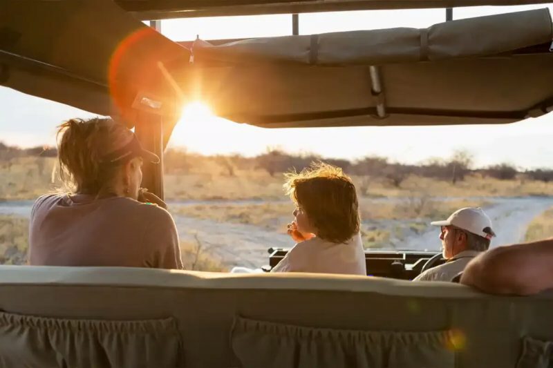 A family watching the plains from an open safari vehicle, the sun low behind them.