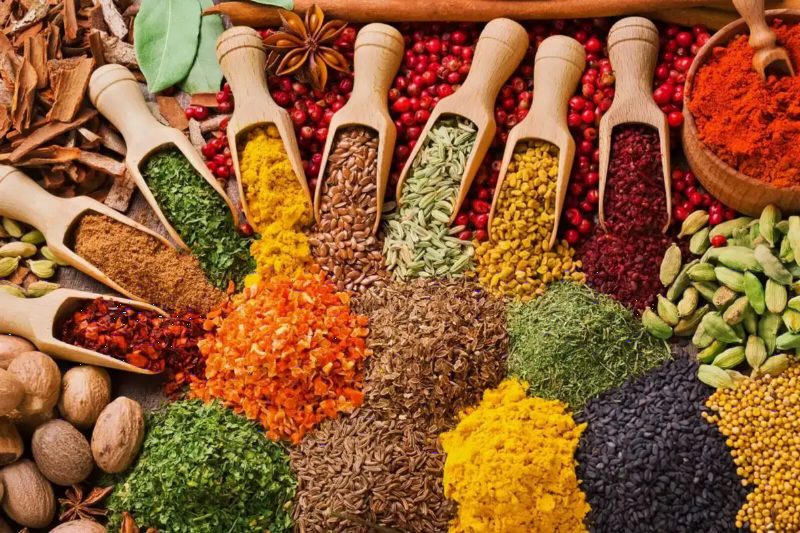 Scoops of whole and ground spices heaped in bright colours.
