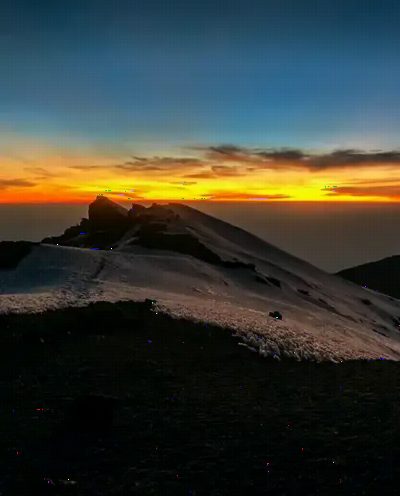 Sunrise from high on Kilimanjaro, an orange band above the cloud and snow on dark volcanic rock.