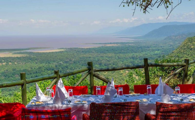 A dining table set with red cloths on a terrace high above the lake and the plains.