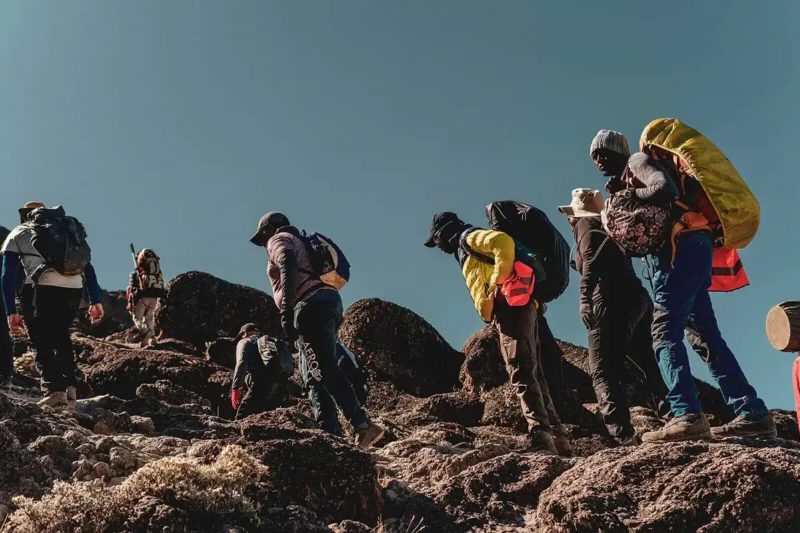 Climbers with heavy packs pausing on rocks high on the mountain.