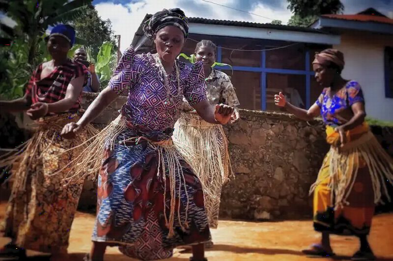 Women in patterned wraps dancing in a village courtyard.