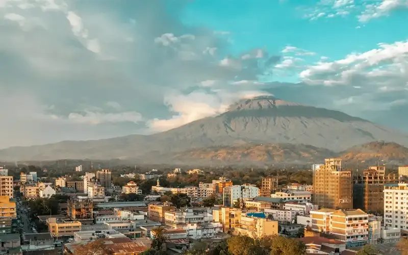 Arusha's rooftops under a blue sky, with Mount Meru rising behind the town.