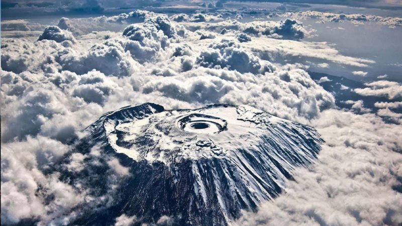 Kilimanjaro from the air, the flat snow-streaked summit and its inner crater rising clear above a deck of cloud.