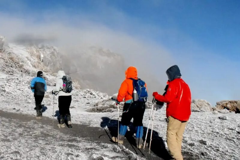 Climbers in heavy jackets walking across snow near the summit.