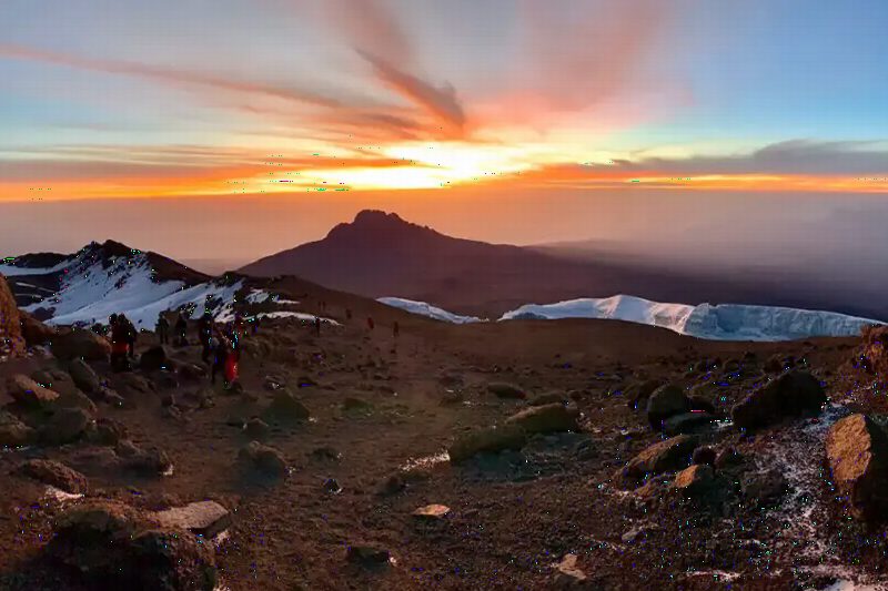 The sun setting behind a jagged peak, seen from high on the mountain's snowy slopes.