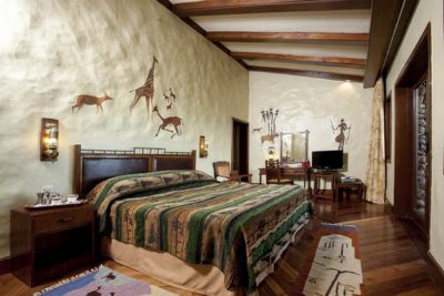A lodge bedroom with a carved wooden bed, striped bedcover and hunting scenes painted directly onto the plaster walls.